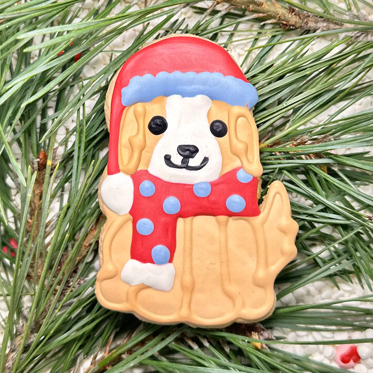Festive dog-shaped cookie wearing a red Santa hat and scarf
